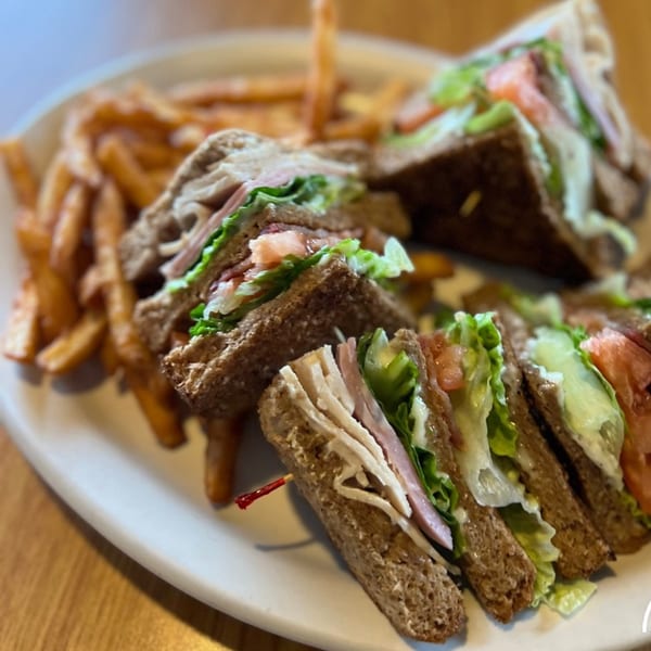 A Mr T's Family Cafe club sandwich with turkey, ham, lettuce, and tomato, served with fries.