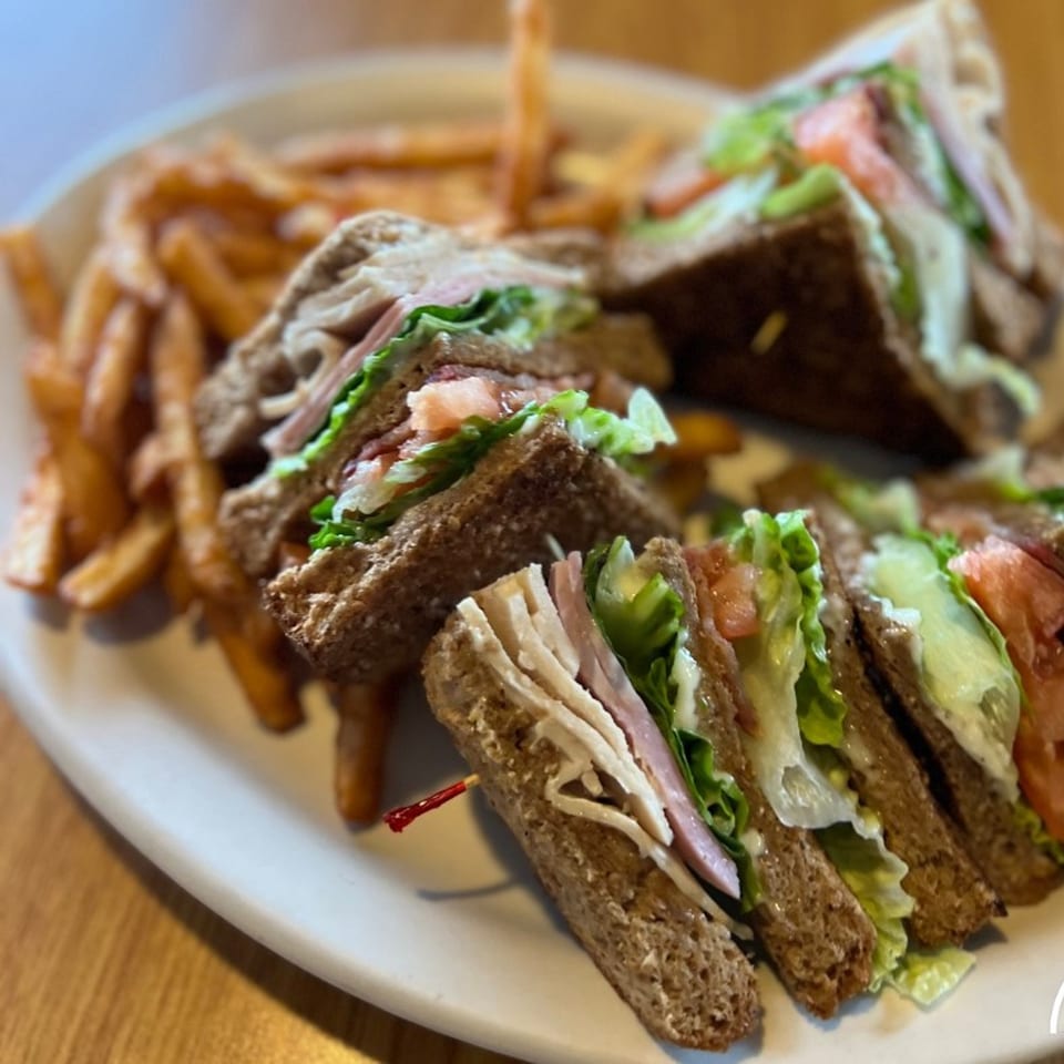 A Mr T's Family Cafe club sandwich with turkey, ham, lettuce, and tomato, served with fries.
