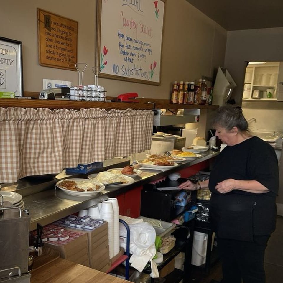 A Mr T's Family Cafe employee prepares American breakfast dishes on a busy kitchen counter.