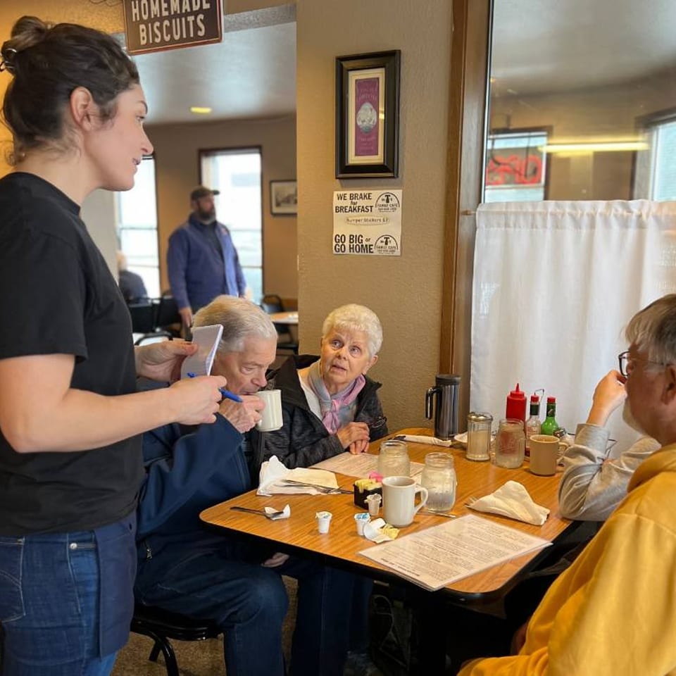 A waitress takes an order from a group of customers seated at a table in Mr T's Family Cafe.