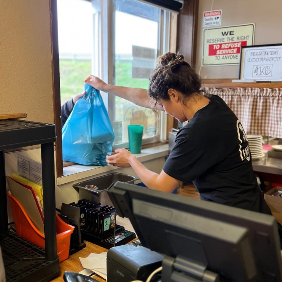 A Mr T's Family Cafe employee hands a blue takeout bag through a window.